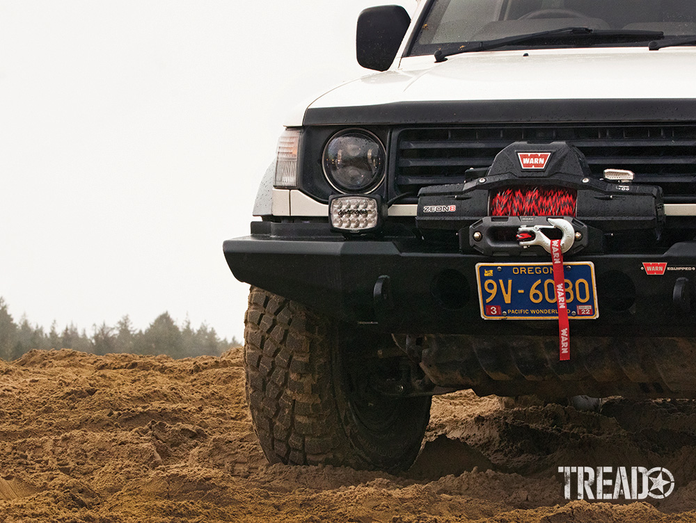 This white 1992 Mitsubishi Pajero is outfitted with a WARN winch bumper, WARN winch, red and black WARN Nightline synthetic rope, and Lightforce aux lights. 