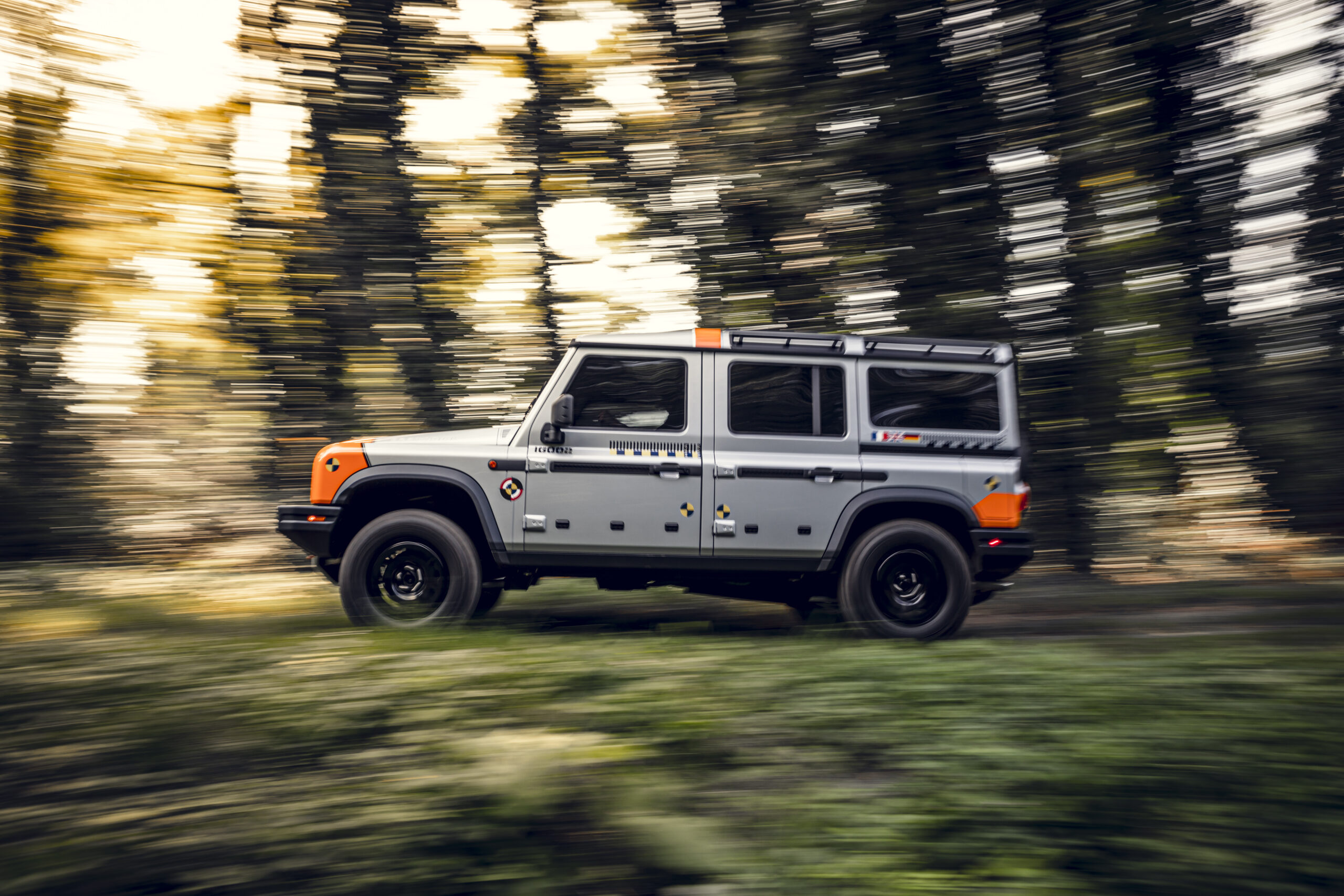 A silver INEOS Grenadier prototype drives quickly through forest roads for testing