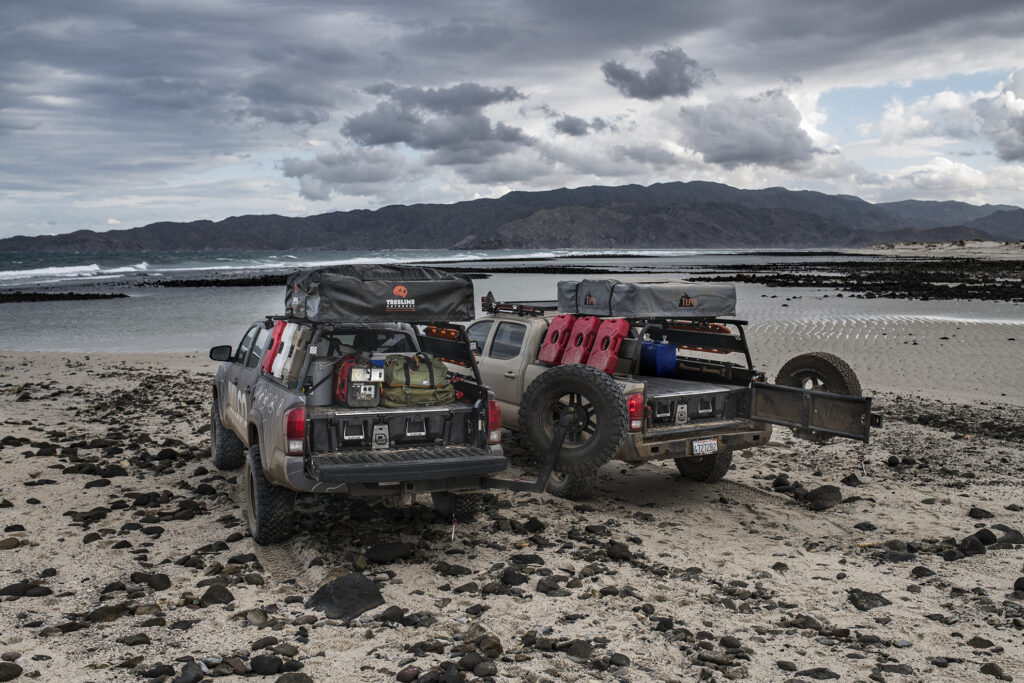 Two trucks parked on beach that have Decked drawer system.