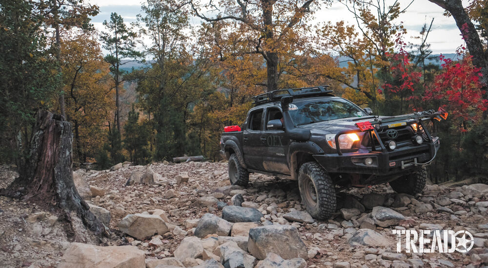 Dark blue Toyota Tacoma drives off road up rocky terrain during Overland Challenge 2020 in Uwharrie National Forest.