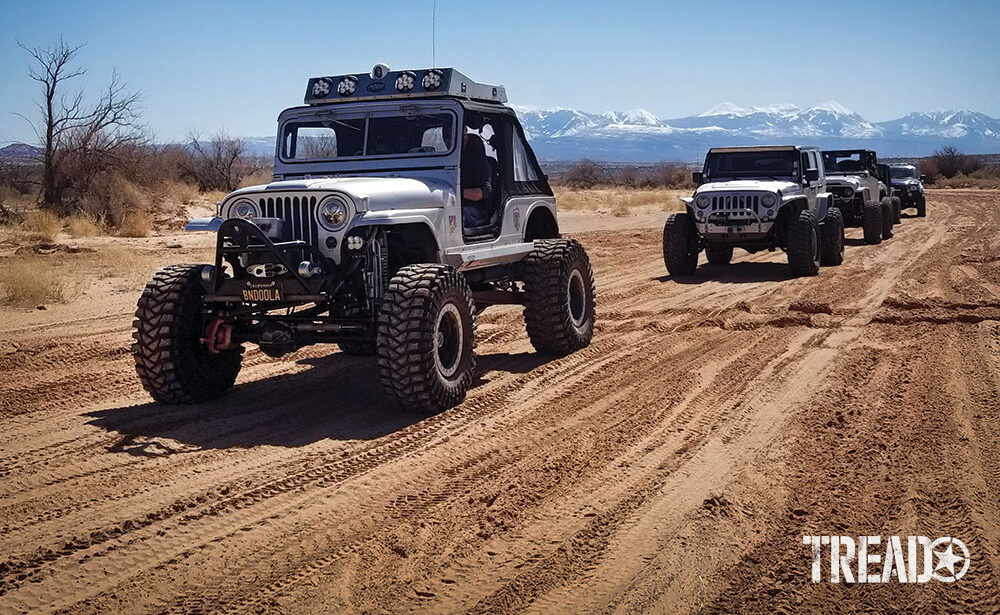 Jeeps drive down a dirt road with a Willys M38A1 leading the group.