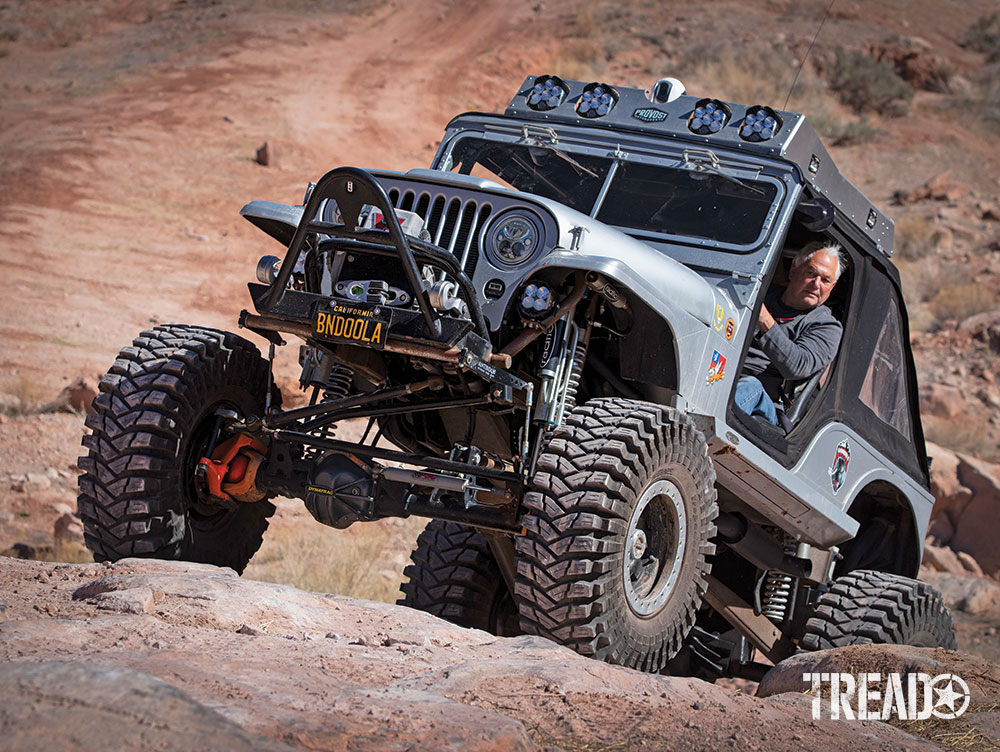 Silver modified Jeep drives up steep rocky terrain in Moab, Utah.