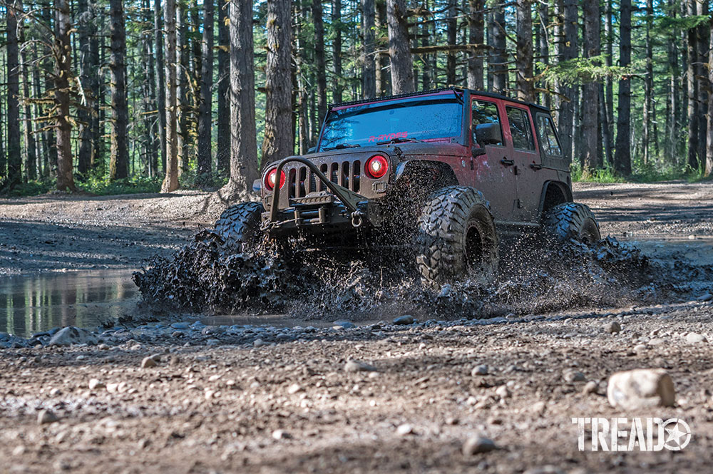 A red 2007 Jeep JKU drives through muddy puddles.