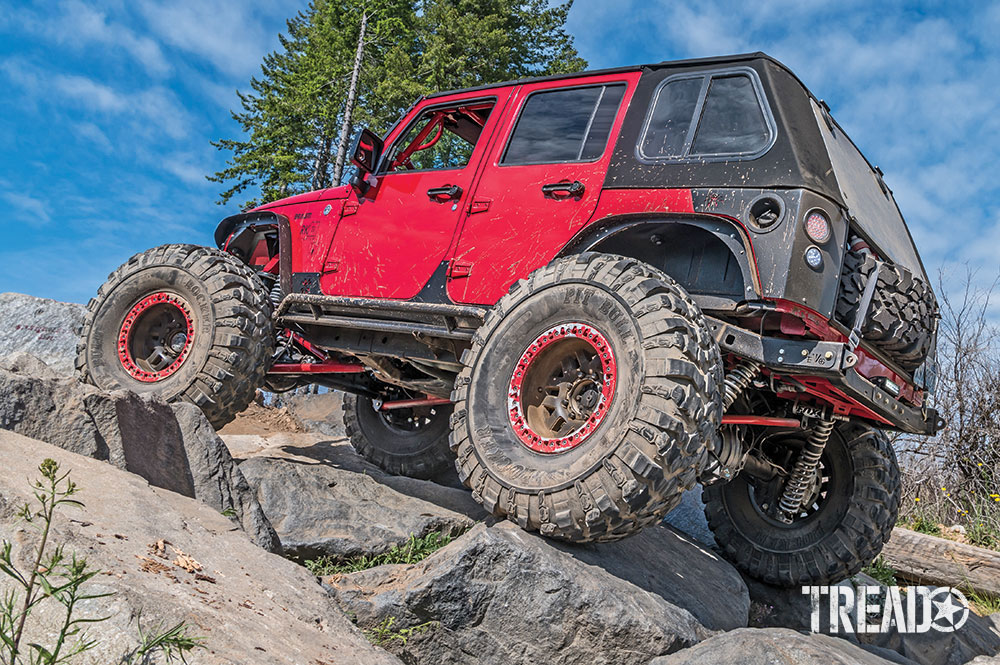 A red Jeep JKU climbs up rocks on an off-road trail.