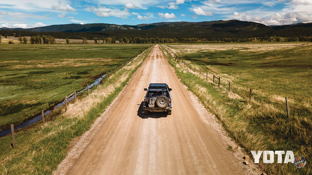 The Lexus LX570 J201 drives down a dirt road with green grass on both sides.