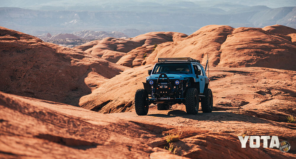 A blue FJ Cruiser drives on the red rocks of Moab, Utah.