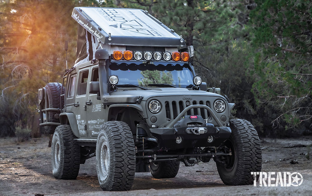 Green overlanding Jeep is parked with pop top camper open.