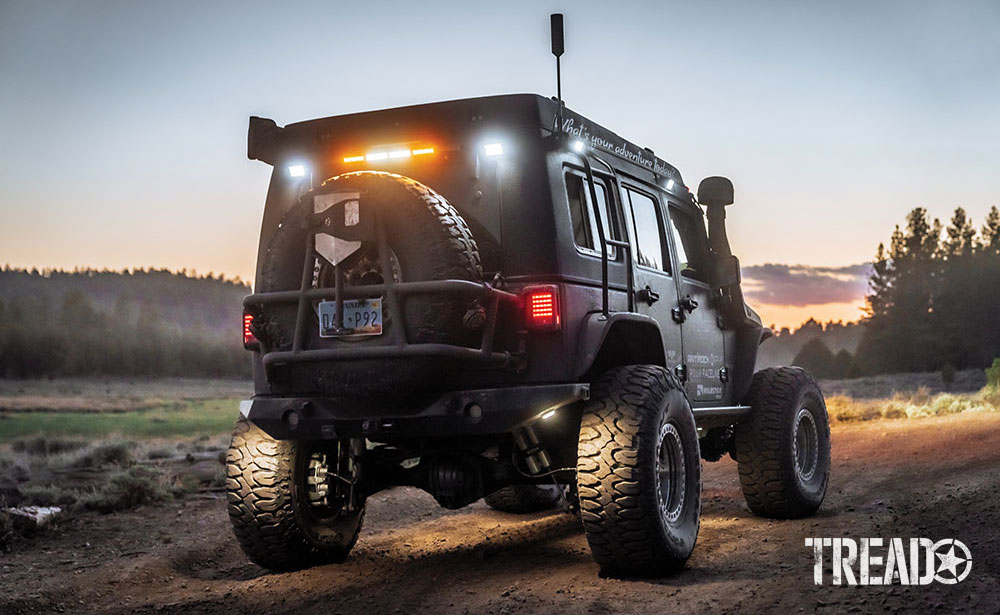 Rear view of green overlanding Jeep with chase lights on at sunset.