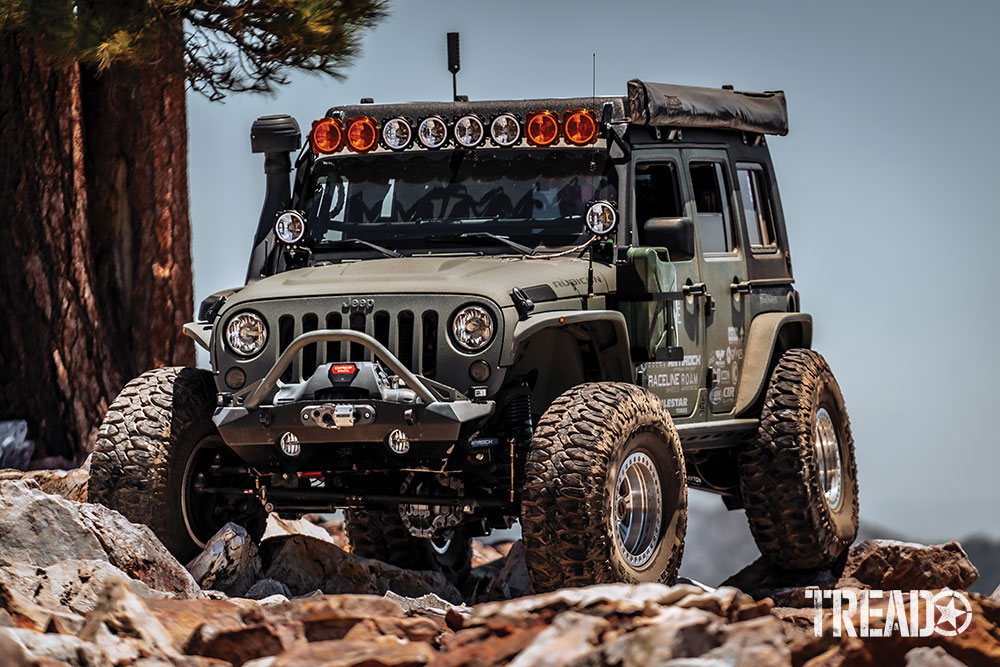 Green Jeep is parked on rocks at top of mountain.