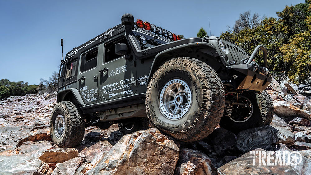 Green overlanding Jeep is parked on rocks.