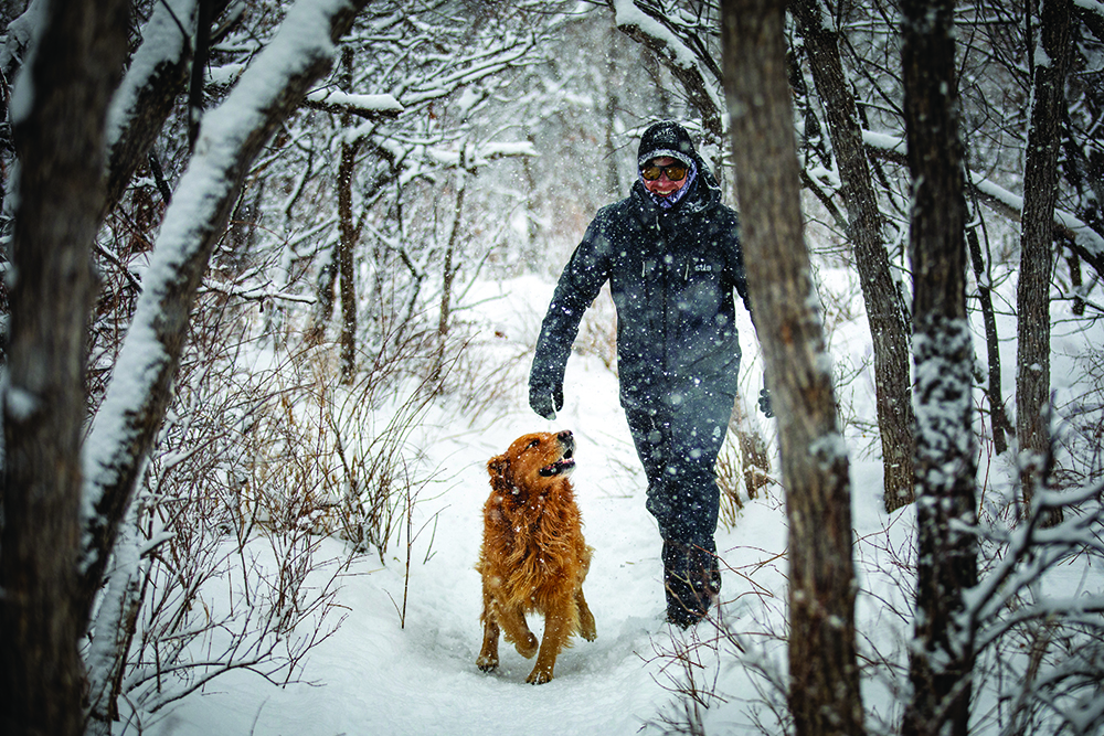 Andrew Muse and his dog, Kicker, walk through the woods in the snow.