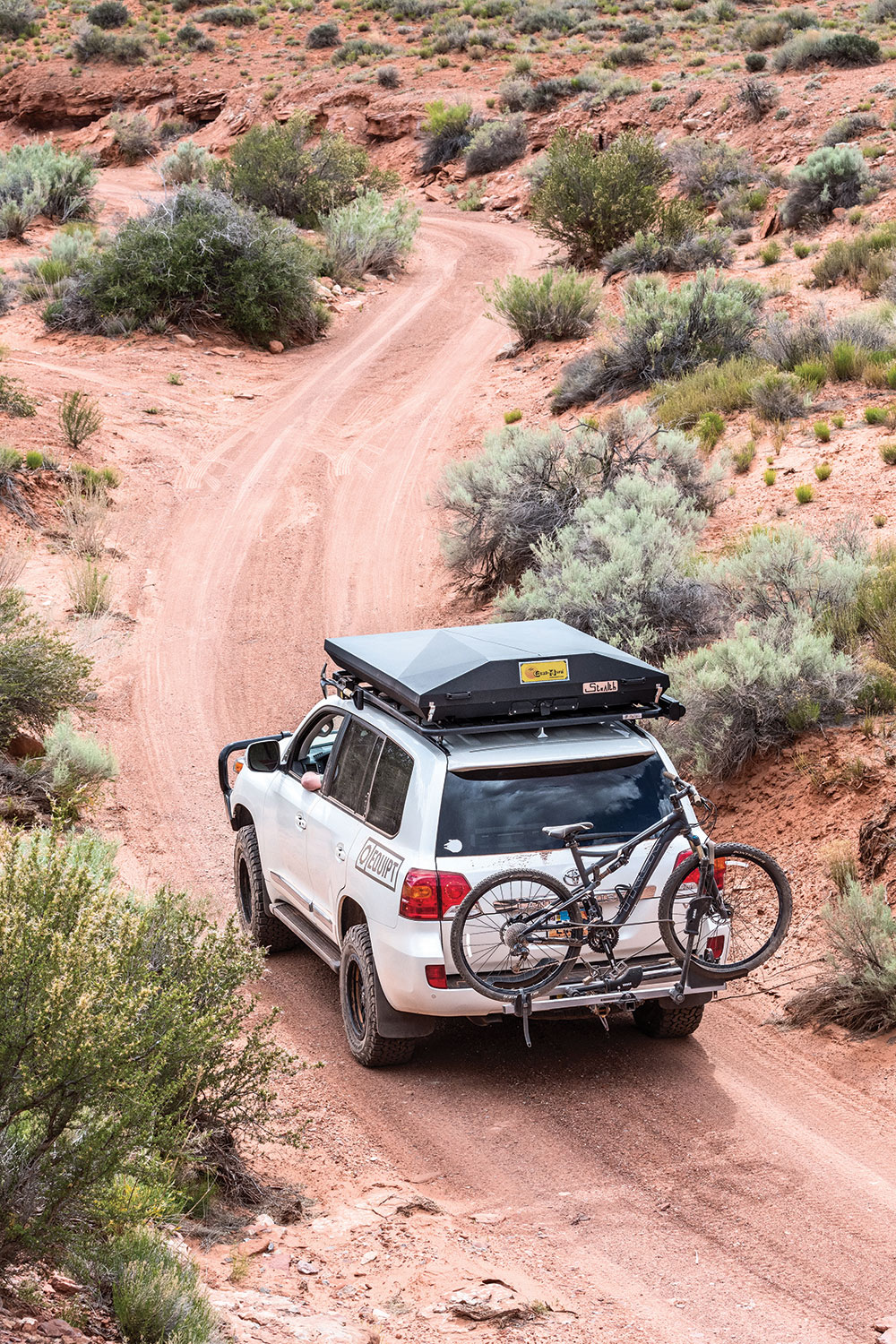 This silver Toyota 4x4 features a roof top tent and rear bumper storage.