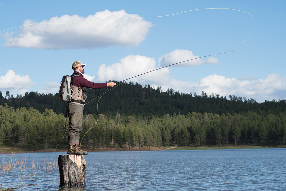 A fly fisherman balances on a log at the edge of the water.