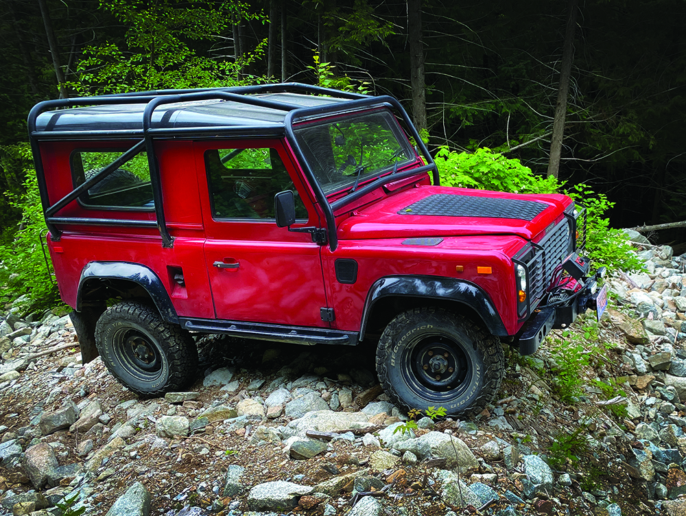 The Defender parked on some rocky forest terrain.