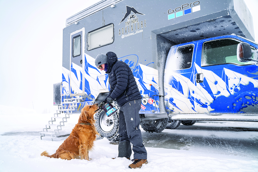 Andrew Muse with his dog, Kicker, standing in the snow in front of the MUSEROAMER