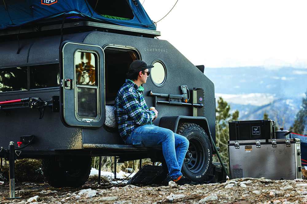 A camper takes in the view from next to the black teardrop camper.