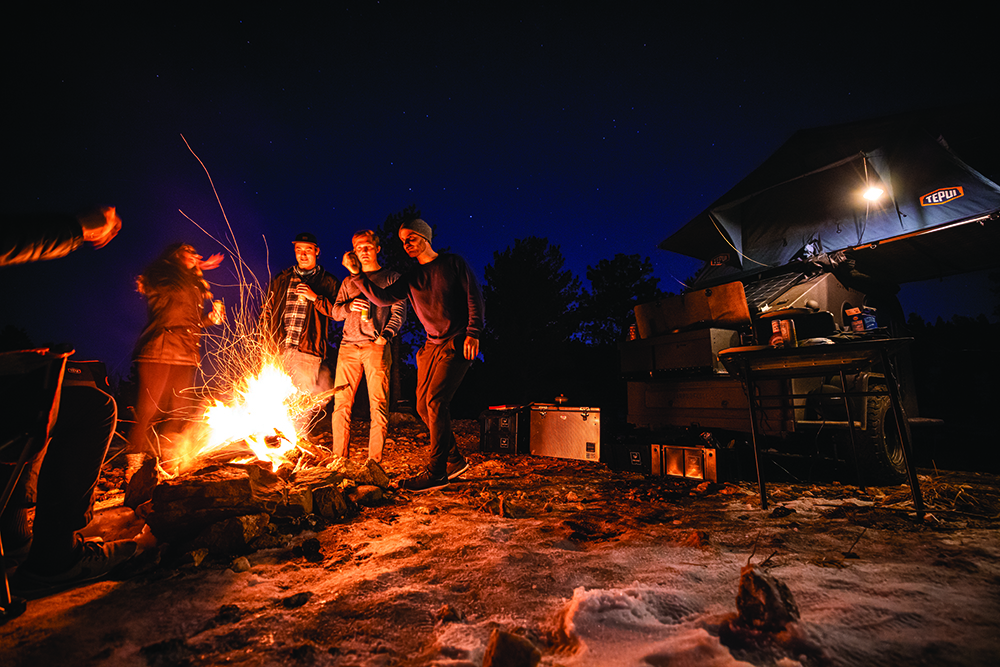 Campers gather around a campfire next to the Campworks NS-1 trailer.
