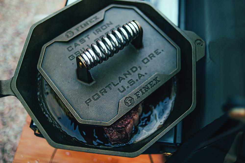 The grill press in use atop a sizzling steak.