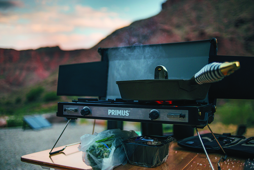 Finex cast iron pan heats up on a small Primus grill with mountain views.