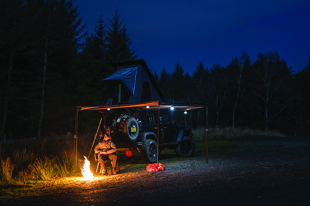 A Jeep and rooftop tent set up by a fire. 