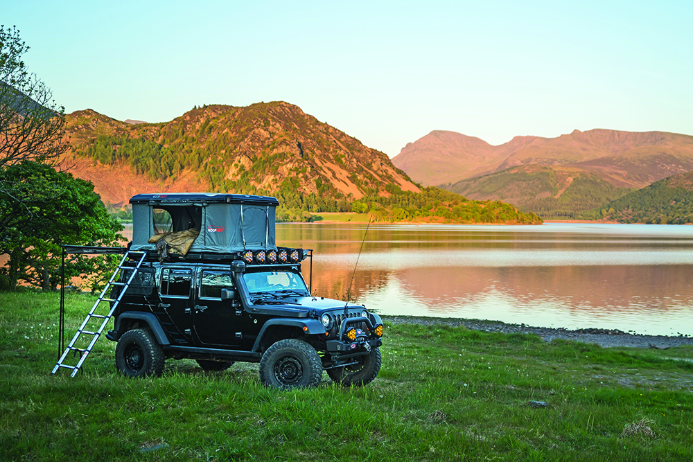 A Jeep and Rooftop Tent camp before a lake. 