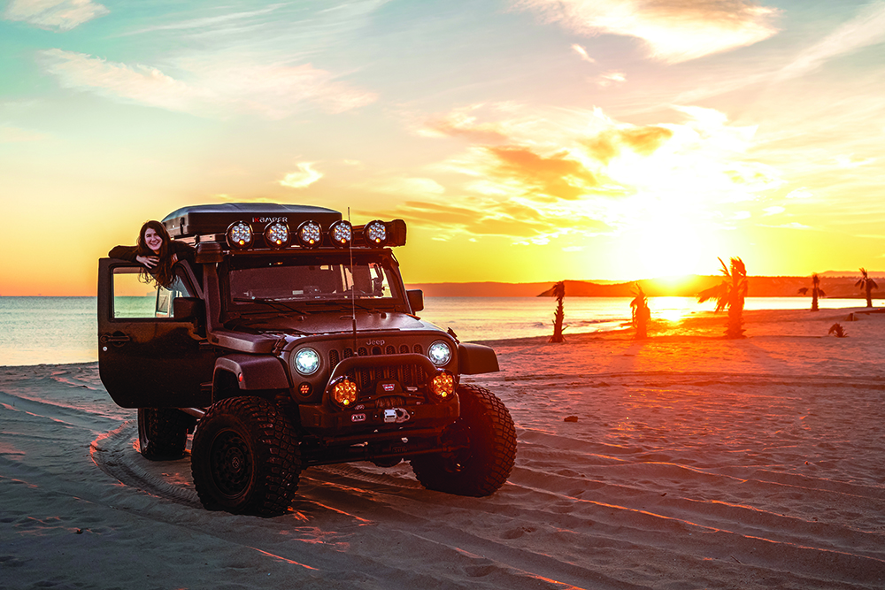 A jeep stands on the beach before the sunset