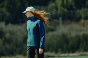 A blonde woman in a hat walks wearing a blue performance jacket.