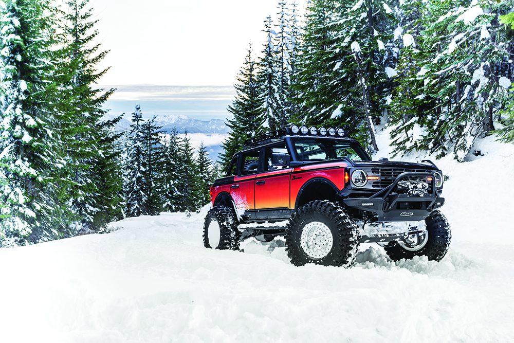 The bright orange Bronco rolls through snow on giant tires.