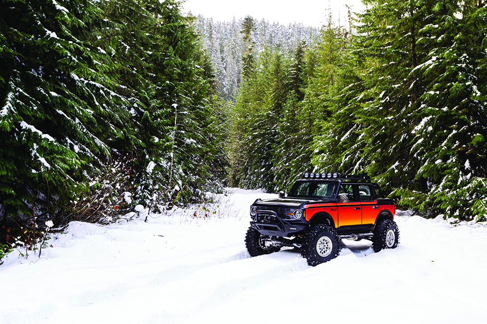 A wide shot of the brightly colored custom Bronco rolling through the snow.