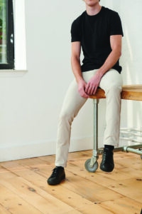 A man wearing khaki pants sits on top of a desk.