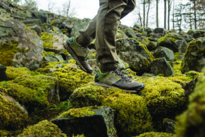 A hiker in waterproof performance sneakers crosses mossy rocks.