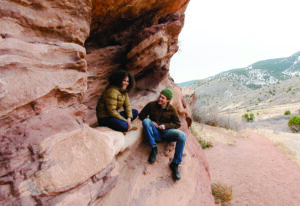Two adventurers in jeans pause to rest on a red rock wall.