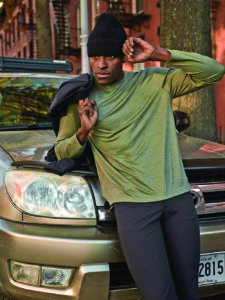 A man in a gree performance long sleeve shirt leans against a gold car.