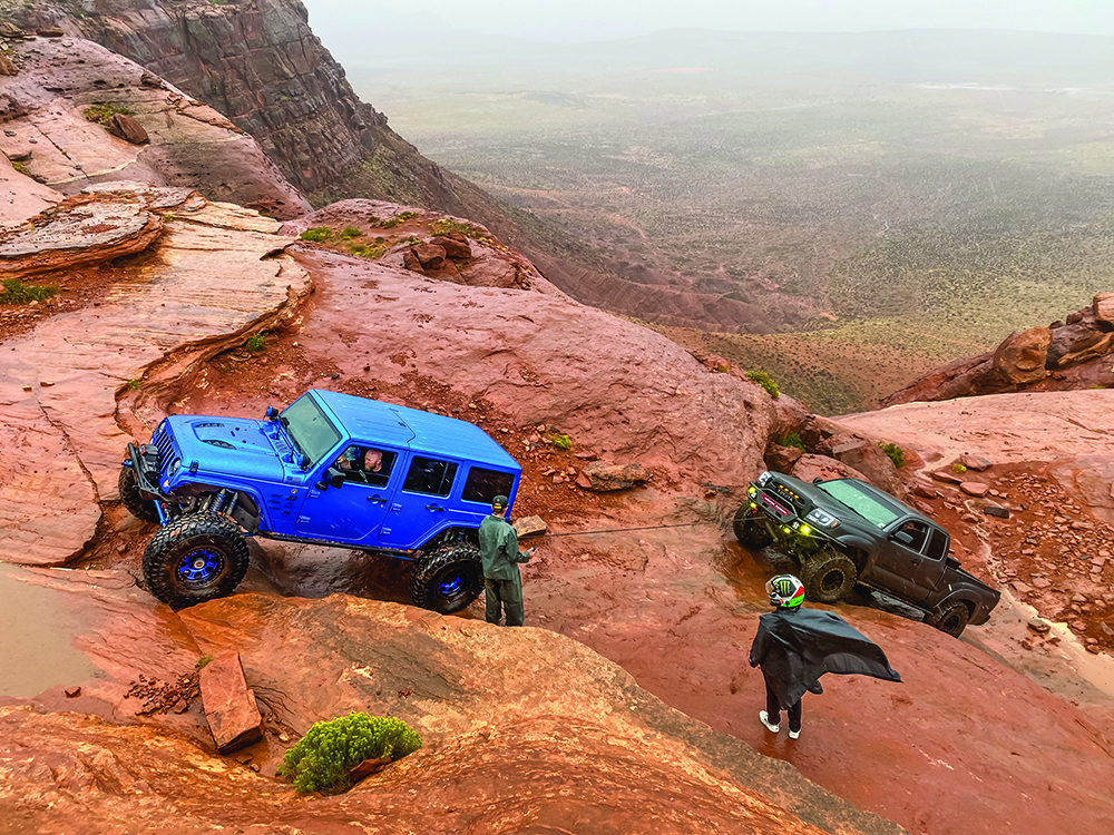 A blue Jeep and black Tacoma follow the red rock trail upward.