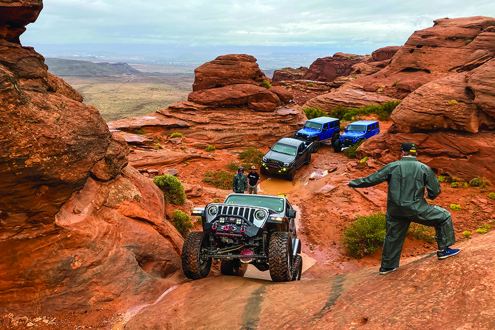 The Jeeps and Tacoma watch as another Jeep drives up an obstacle.