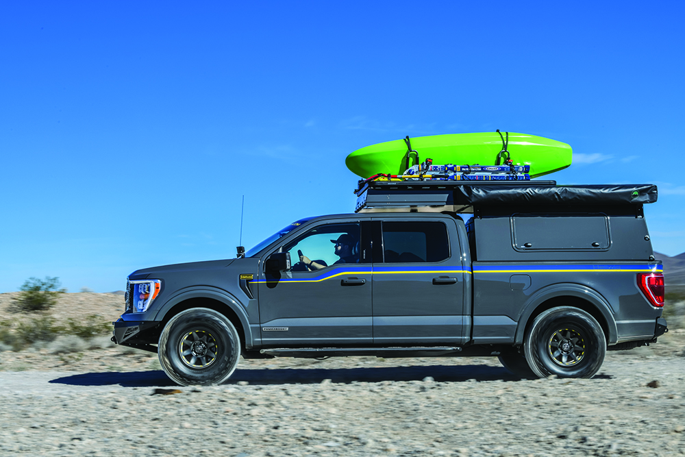 A full-body side shot of this gray F-150 with blue and yellow decorative stripes and green kayak mounted on the roof.