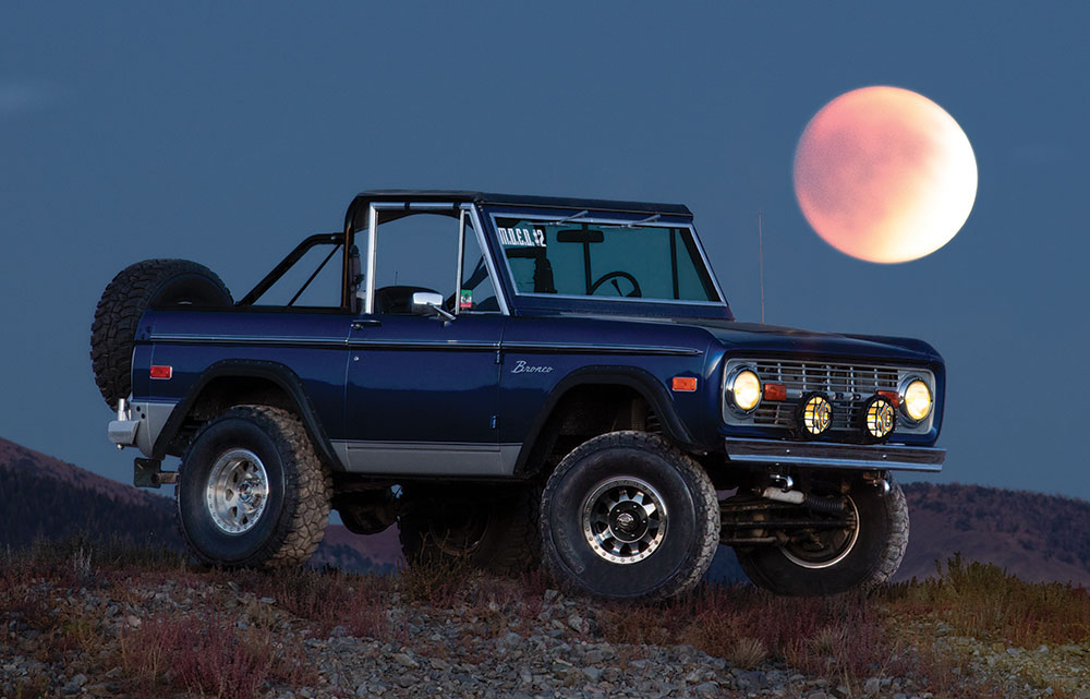 A closer shot of the same car under the moon, which now appears larger thanks to photography techniques.