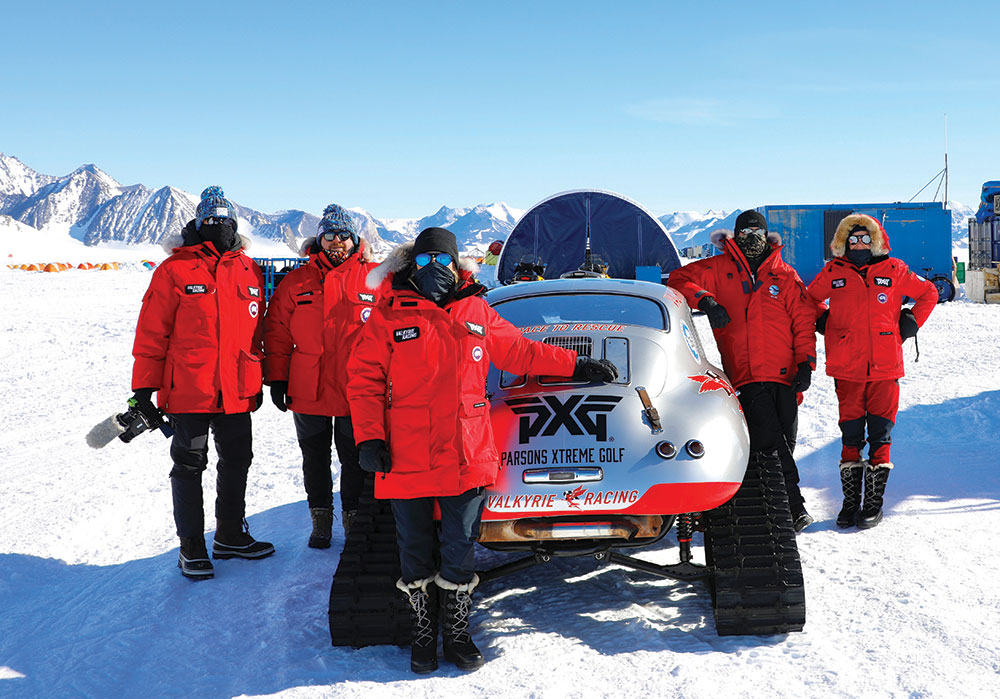 The five members of the Valkrie Racing team pose in red coats in front of the gray Porsche 356.