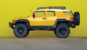 A mini yellow FJ Cruiser parked on concrete in front of a yellow wall.