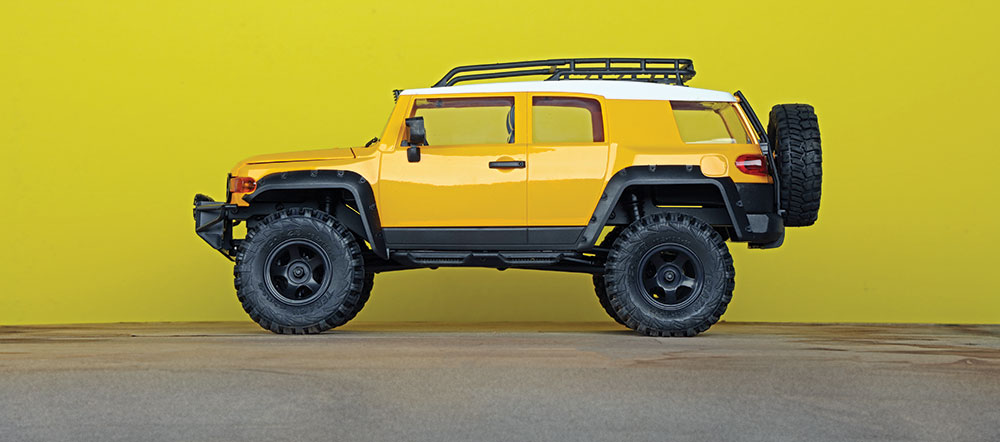 A mini yellow FJ Cruiser parked on concrete in front of a yellow wall.