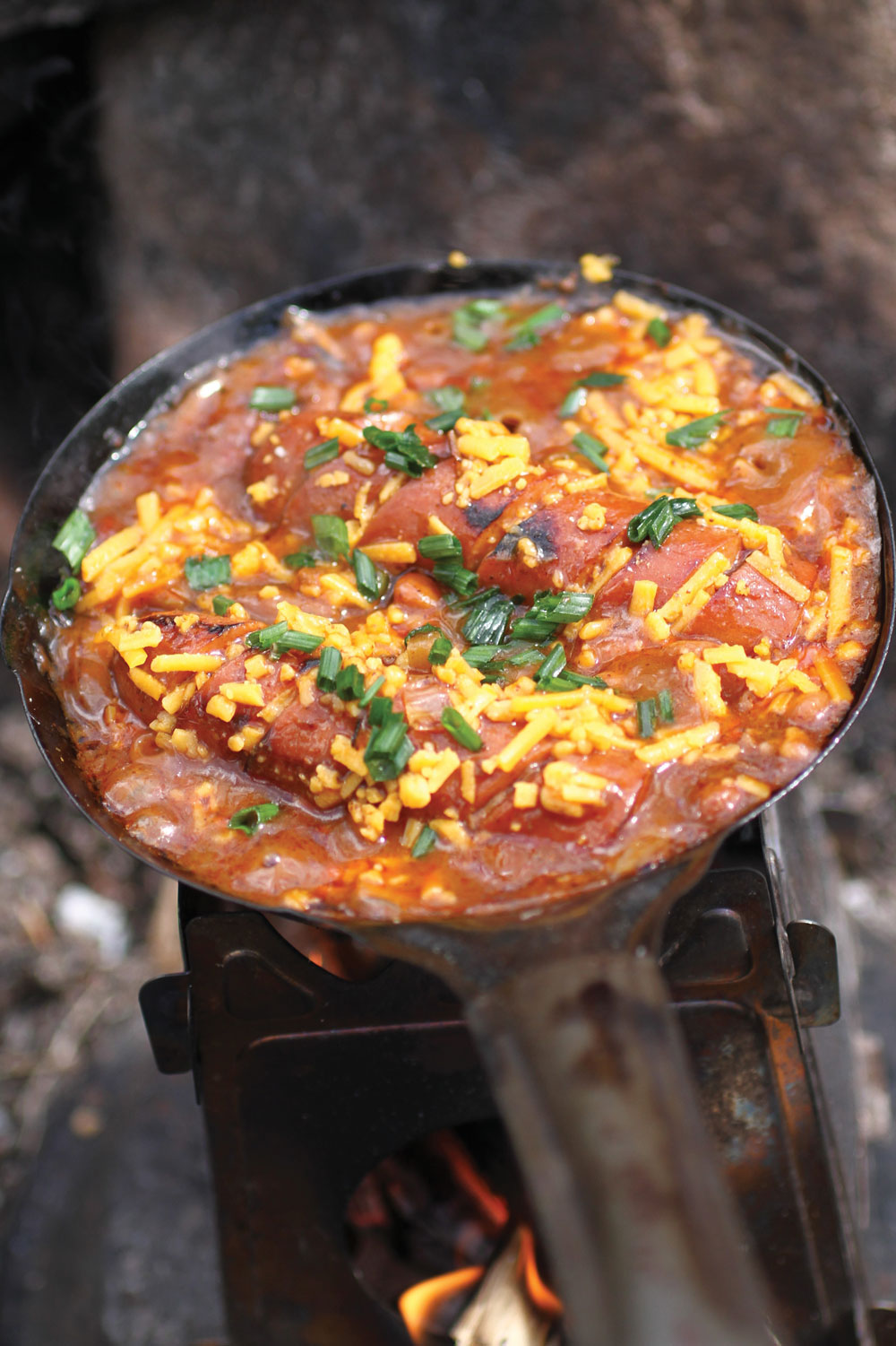 Chili-cheese hot dog skillet cooks over a campsite flame.
