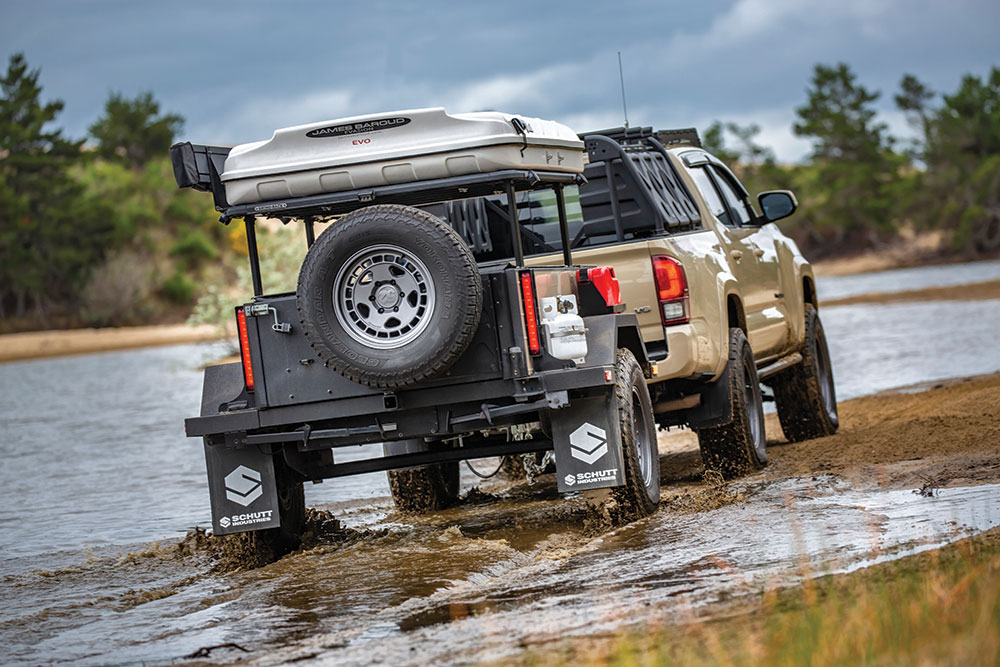 The Tacoma and trailer roll through muddy water.