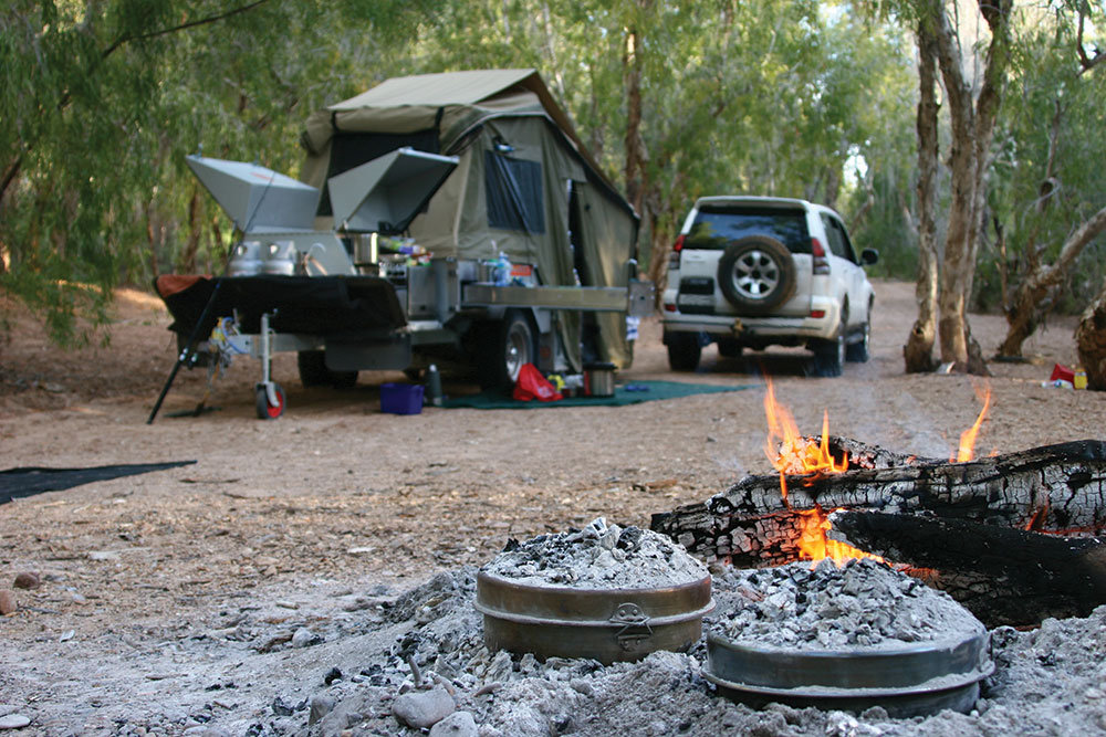 Two trucks parked in a camp setup next to a cooking fire.
