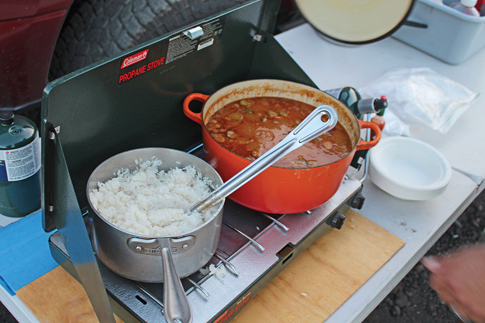 Two pots hold rice and jambalaya on a green camp stove.