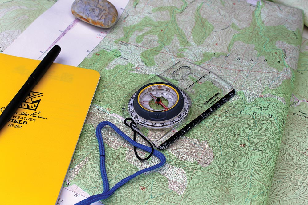 Green topographic map and compass with yellow notebook.