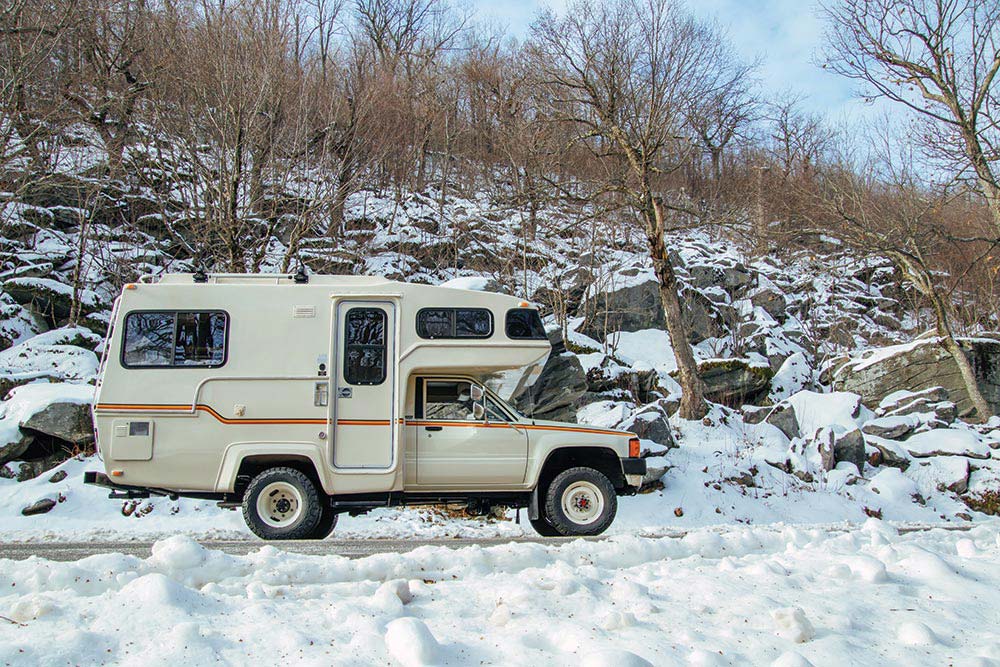 The boxy off-white camper looks at home in the snowy mountains.