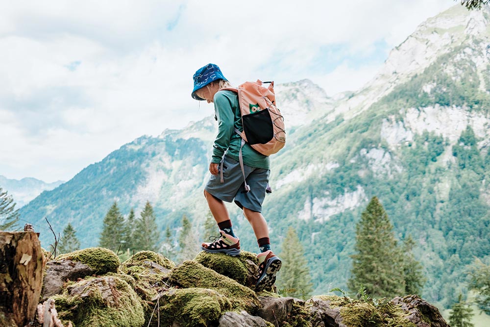 a Child with a backpack climbing on some rocks with mountains in the backround - family gear 