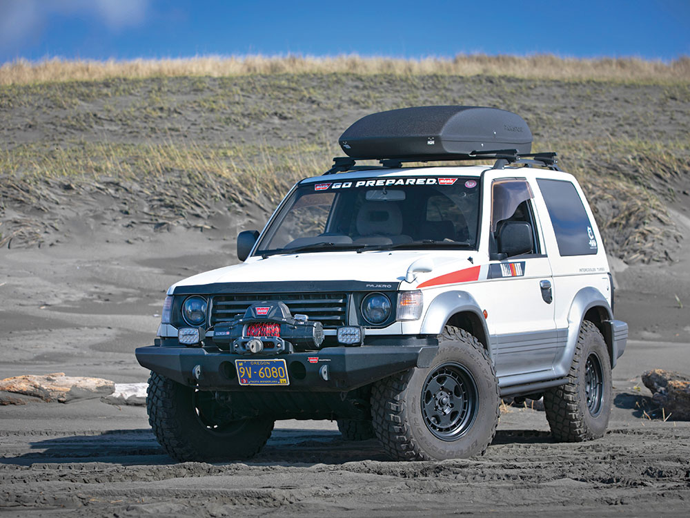 A white vehicle with upgrades like red details and a black box on the rooftop parks on a muddy field.