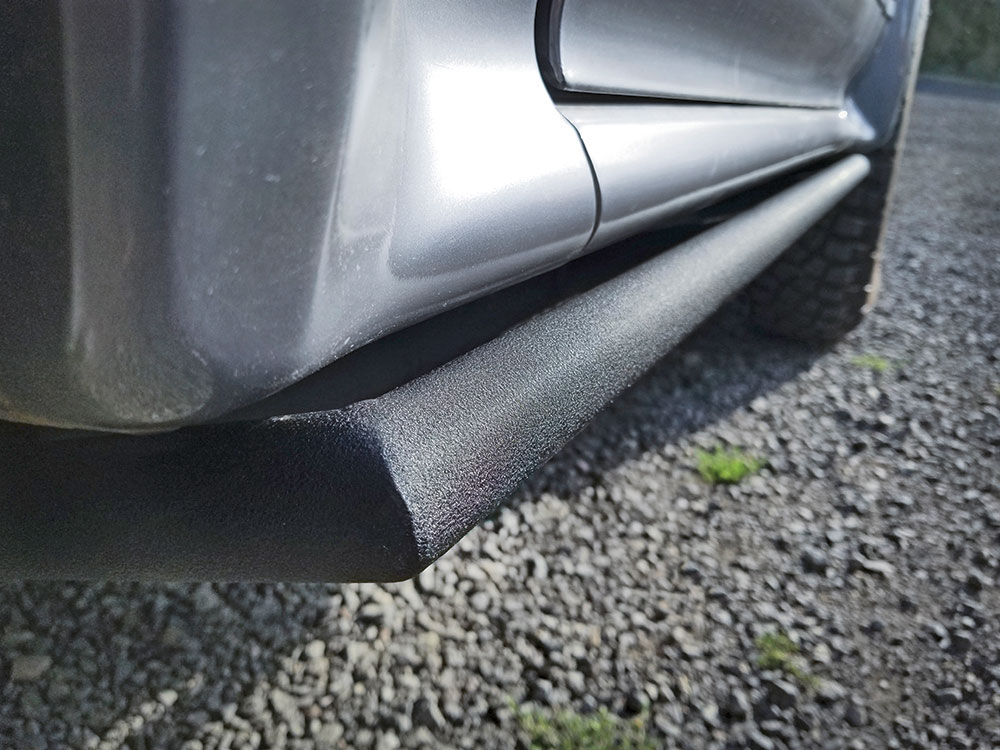 A close up view of black powedercoated rock sliders on a gray vehicle.