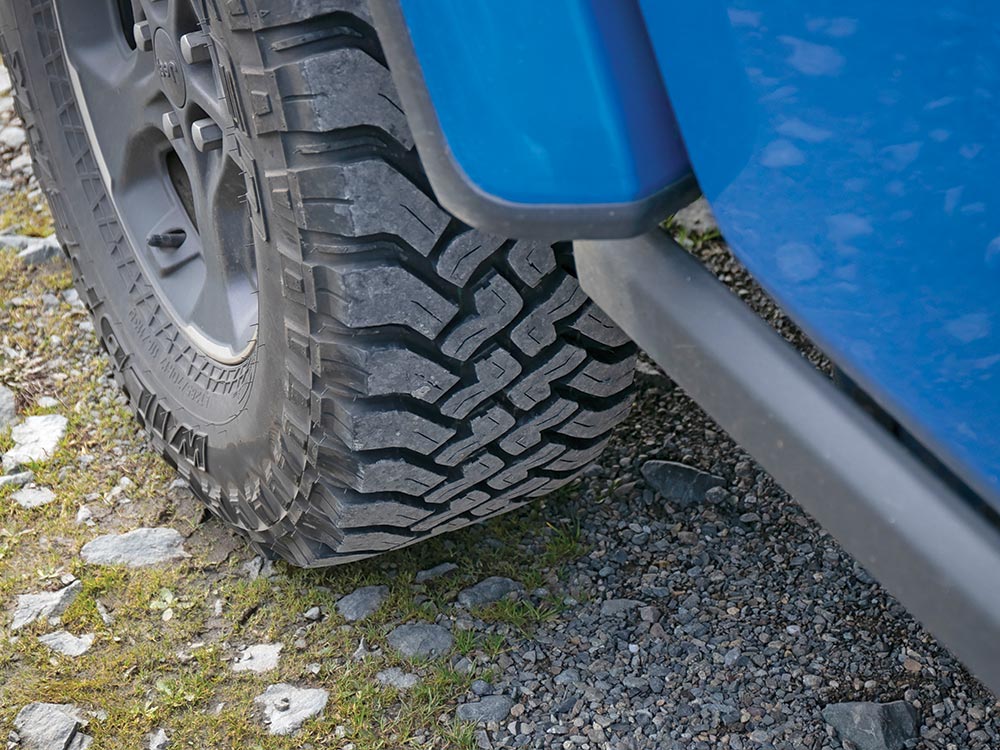 The tread stands out on the tires of this blue vehicle as it drives over gravel and grass.
